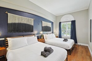 Ein Hotelzimmer mit zwei Betten, einem großen Fenster mit Vorhängen, einem Deckenventilator und einem Wandbild.