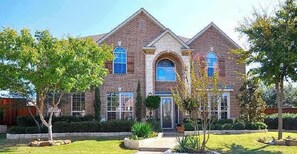 A two-story house with a brick facade, a central arched window, and a symmetrical design. - 5BD DFW Mansion - Pool, Cinema, Games (Plano)
