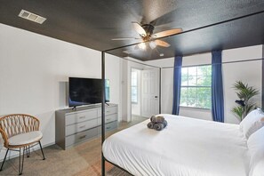 Un dormitorio con cama, televisor, ventilador de techo, silla y cómoda.