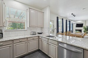 A modern kitchen with a granite countertop, stainless steel appliances, and a dining area with a table and chairs. - Colonial Style Retreat ft Pool, Cinema, Jacuzzi (Fort Worth)