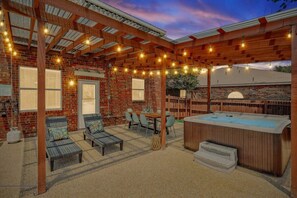 Un patio cubierto con mobiliario, un jacuzzi y luces colgantes.