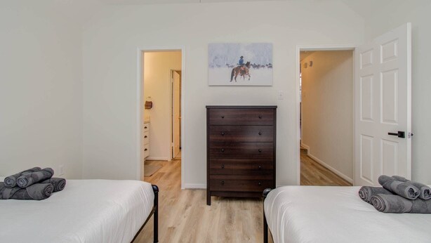 Quarto com duas camas, penteadeira de madeira, um quadro e porta para outro cômodo.