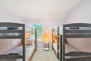 Una habitación con literas, una mesita de noche pequeña con una lámpara y un cuadro de una jirafa en la pared.