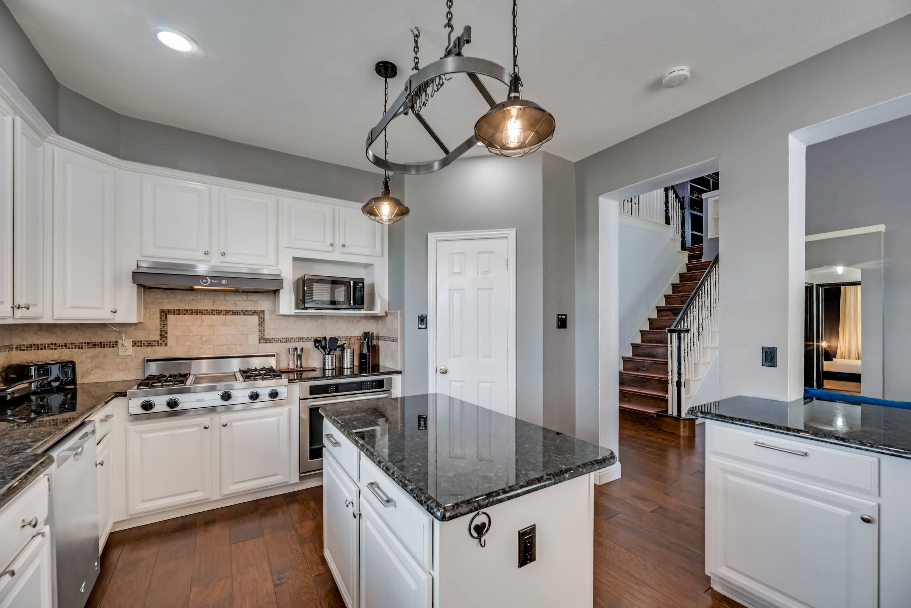 A modern kitchen with white cabinets, a large island, stainless steel appliances, and a unique chandelier.