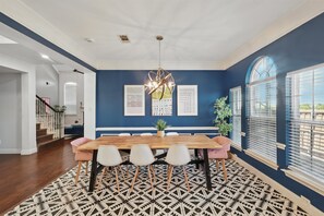 Uma sala de jantar com mesa de madeira, cadeiras brancas, tapete estampado e parede azul.