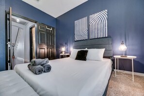Quarto de hotel com cama, duas mesas de cabeceira com luminárias, uma porta e uma parede com arte abstrata.