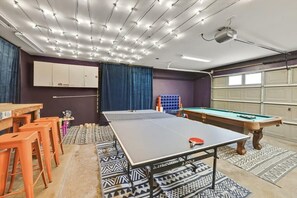 Ein Raum mit Tischtennisplatte, Billardtisch und Barhocker.