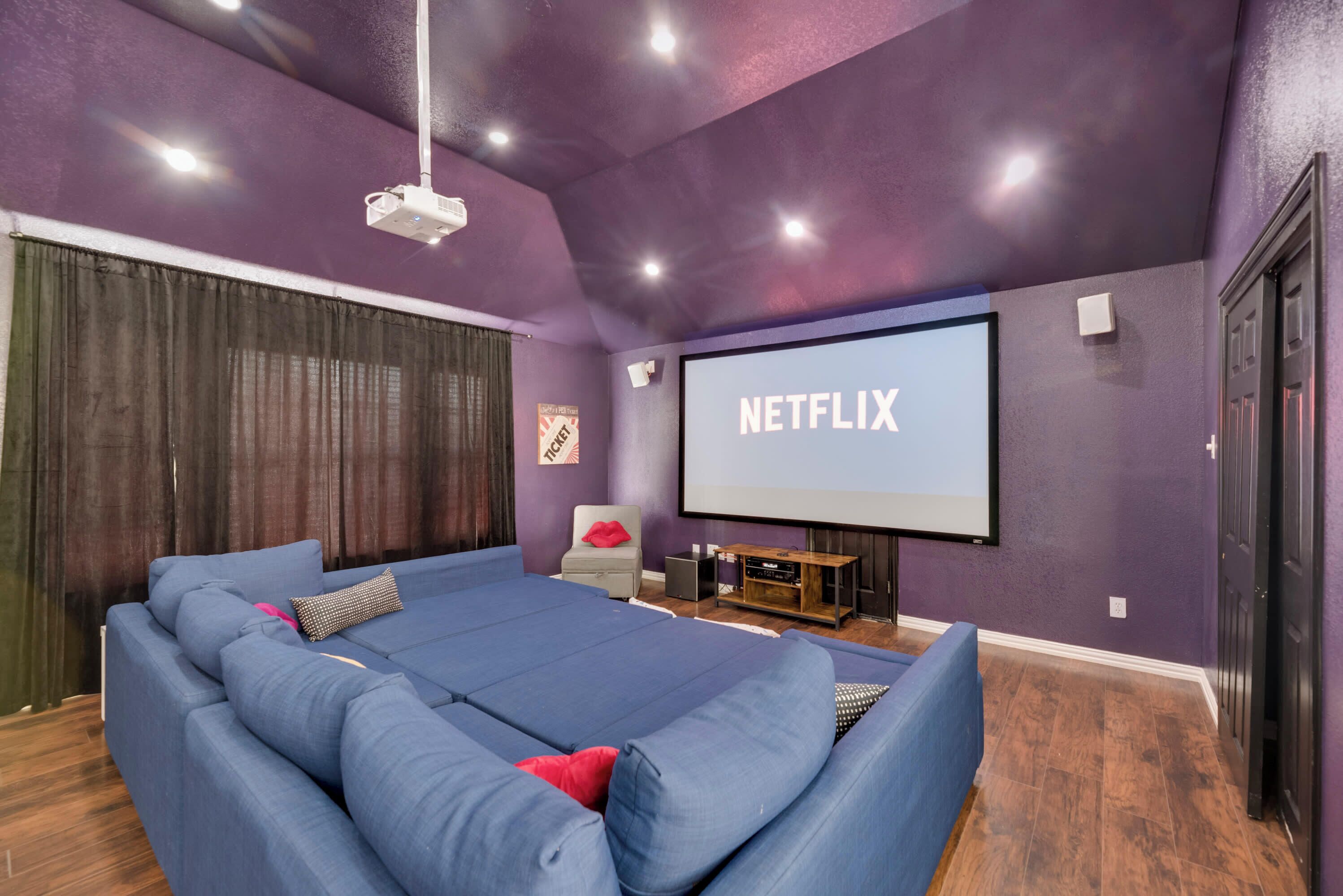 A home theater with a large screen, blue seating, and a projector.
