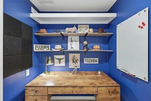 Une pièce avec un bureau en bois, des murs bleus, des étagères blanches ornées d’objets décoratifs, un tableau blanc et un globe terrestre fixé au mur.