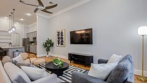 A modern living room with a sofa set, a coffee table, a flat-screen TV, and a ceiling fan. - High End In The Center - Mins to Downtown w Pool (Houston)