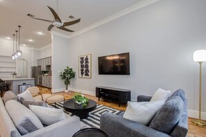 A modern living room with a sofa set, a coffee table, a flat-screen TV, and a ceiling fan. - High End In The Center - Mins to Downtown w Pool (Houston)