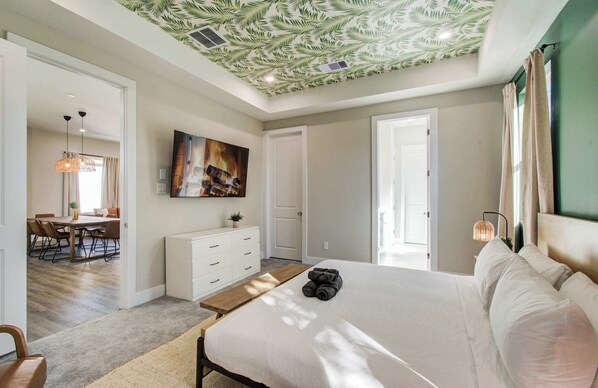 A bedroom with a bed, a desk, a chair, a painting, and a ceiling with a leaf pattern. - Chic & Central 3-bd/2.5-ba, Mins to DT & Midtown (Houston)