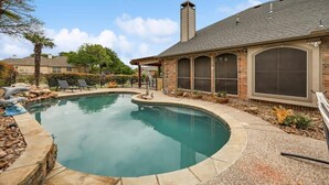 A swimming pool with a curved edge, surrounded by a patio area with a pergola and lounge chairs. - Stunning 6br, Pool - Great for Big Groups (Rowlett)