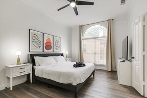 A modern bedroom with a bed, bedside tables, a ceiling fan, and artwork on the wall. - Stunning 6br, Pool - Great for Big Groups (Rowlett)