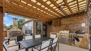 An outdoor patio with a brick fireplace, a grill, and a table with chairs. - Stunning 6br, Pool - Great for Big Groups (Rowlett)
