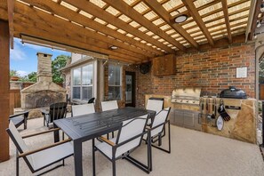An outdoor patio with a brick wall, a grill, and a table with chairs. - Stunning 6br, Pool - Great for Big Groups (Rowlett)