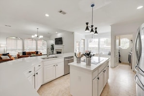 A modern kitchen with white cabinetry, a large island, and a dining area with a sofa and table. - Stunning 6br, Pool - Great for Big Groups (Rowlett)