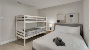A bedroom with a bunk bed, a single bed, a bedside table with a lamp, and two framed pictures on the wall. - Gorgeous Sunny Home for Big Groups w/ Private Pool (Garland)