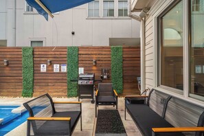 A patio area with a pool, outdoor seating, a grill, and a wooden wall with greenery. - Houston Centrally Located w/ Backyard Pool Retreat (Houston)