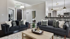 Ein modernes Wohnzimmer mit zwei dunkelgrauen Sofas, einem Holztisch und einer Küchenzeile mit weißen Schränken und Edelstahlgeräten.