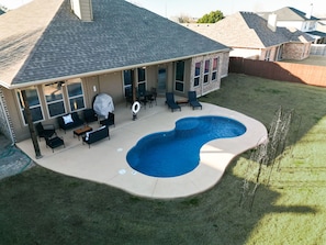 A residential backyard with a swimming pool, outdoor furniture, and a covered patio area. - 5-bed/2-bath Pool & Backyard Retreat (Waxahachie)