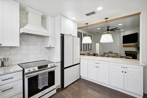 A modern kitchen with white cabinetry, a stainless steel stove, and a black refrigerator. - Allen Abode - 4 Bedrm. Pool, Fire Pit , Charm (Allen)