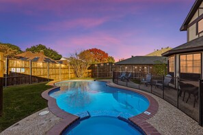 A backyard with a swimming pool, a wooden fence, and a patio area with chairs. - Prime Plano 4BR Home With Pool, Arcarde, Ping-pong (Plano)