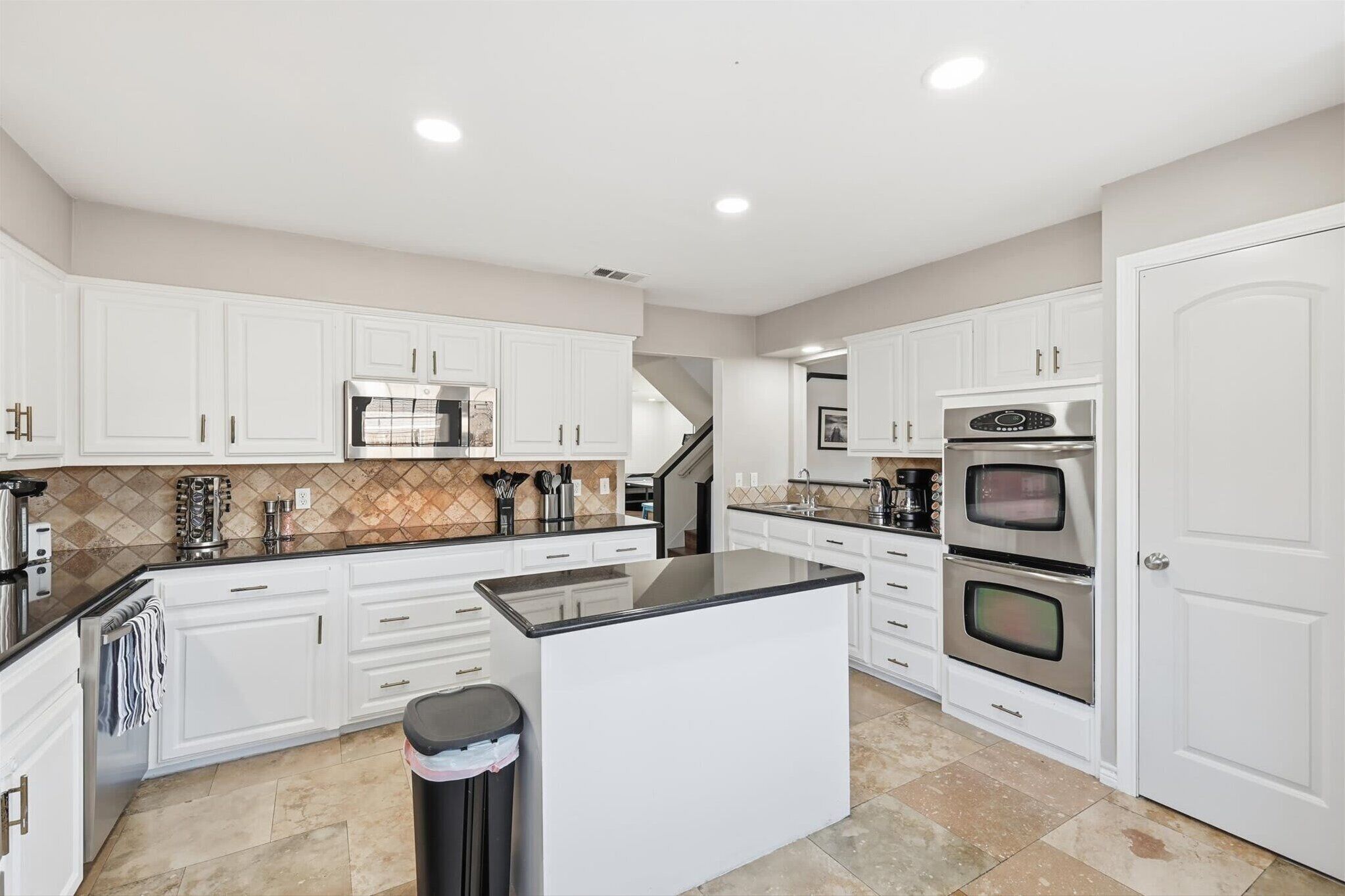 A spacious kitchen with white cabinets, a central island, stainless steel appliances, and a tiled backsplash.
