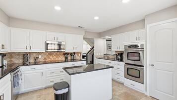 A spacious kitchen with white cabinets, a central island, stainless steel appliances, and a tiled backsplash.
