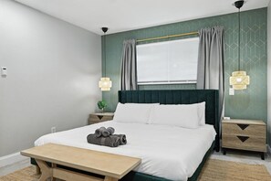 Habitación de hotel ordenada con cama, mesitas de noche, lámparas, ventana con cortinas y una planta pequeña.