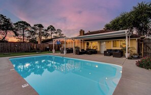 Ein Garten mit Swimmingpool, Sitzgelegenheiten im Freien und einer überdachten Terrasse.