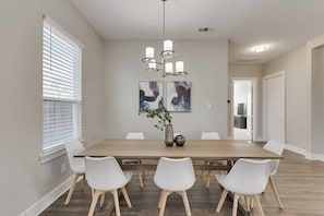 A dining area with a long wooden table, white chairs, a chandelier, and abstract art on the wall. - Modern and Spacious High End Home Near Downtown (Dallas)