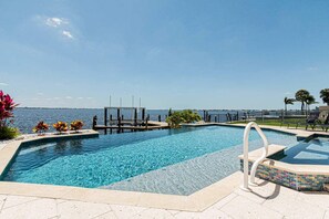 A swimming pool with a view of the sea, a dock, and lounge chairs. - Breathtaking 6BD Riverfront Mansion w Pool (Cape Coral)