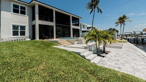 A modern two-story house with a swimming pool, palm trees, and a waterfront view. - Breathtaking 6BD Riverfront Mansion w Pool (Cape Coral)