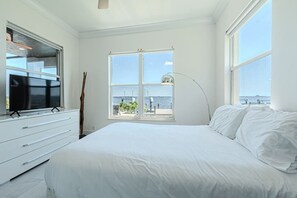 A bedroom with a large bed, a TV, a window with a view of the sea, and a lamp. - Breathtaking 6BD Riverfront Mansion w Pool (Cape Coral)