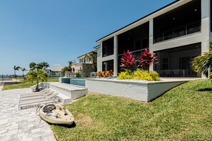 A modern house with a pool, a boat, and a well-maintained lawn. - Breathtaking 6BD Riverfront Mansion w Pool (Cape Coral)
