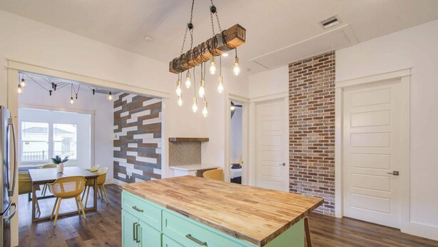 A kitchen with a wooden island, green cabinets, and a brick accent wall. - 3BD Historic Charm x Modern Amenities w Hot Tub (Houston)