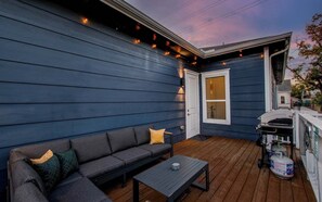 Eine Terrasse mit einer Couch, einem Tisch, einem Grill und einem Gasbehälter.
