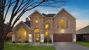 A two-story brick house with a garage, large arched windows, and a well-maintained lawn. - 5-bd Vacation Retreat w Pool & Ping Pong! (Fort Worth)