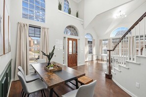 A spacious room with a wooden dining table, chairs, a staircase, and large windows. - 5-bd Vacation Retreat w Pool & Ping Pong! (Fort Worth)