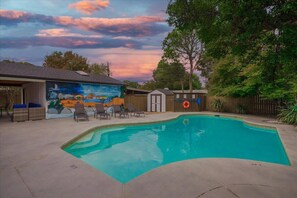 Ein Pool mit Wandmalerei, Liegestühlen und einem überdachten Bereich mit Wandgemälde.