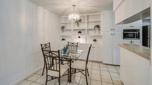 A compact kitchen with white cabinetry, a dining table with chairs, and a hanging plant. - Heart of Houston - 3-bd Apartment (Houston)
