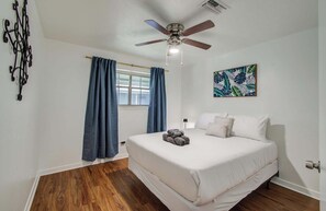 Ein Schlafzimmer mit einem Bett, einem Deckenventilator, einem Fenster mit Vorhängen, einem Wandbild und einem Holzboden.