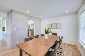Ein stilvolles Esszimmer mit einem langen Holztisch, Stühlen, einer Vase mit Pflanze und gerahmten Kunstwerken an der Wand.