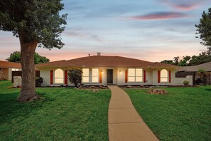 A residential house with a front yard, a pathway leading to the entrance, and a large tree on the left. - 5BR Near At&t Stadium Pool, Hot Tub, Mini Golf (DeSoto)