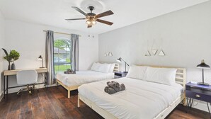 Un dormitorio con dos camas, un escritorio, una silla, un ventilador de techo y una ventana con cortinas.