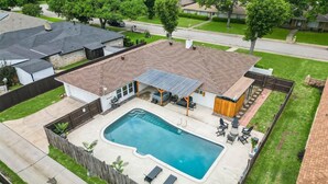 Un patio trasero residencial con piscina, mobiliario de patio y una zona de estar cubierta al aire libre.