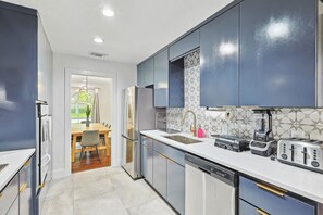 Una cocina moderna con electrodomésticos de acero inoxidable, lavavajillas y una encimera con licuadora y tostadora.