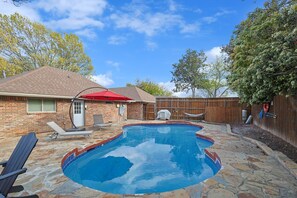 Ein Garten mit Swimmingpool, einem Ziegelhaus, einem Holzzaun und einer Hängematte.