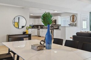 Eine moderne Küche mit weißen Schränken, einem Esstisch mit Stühlen und einer blauen Vase mit einem grünen Blatt.